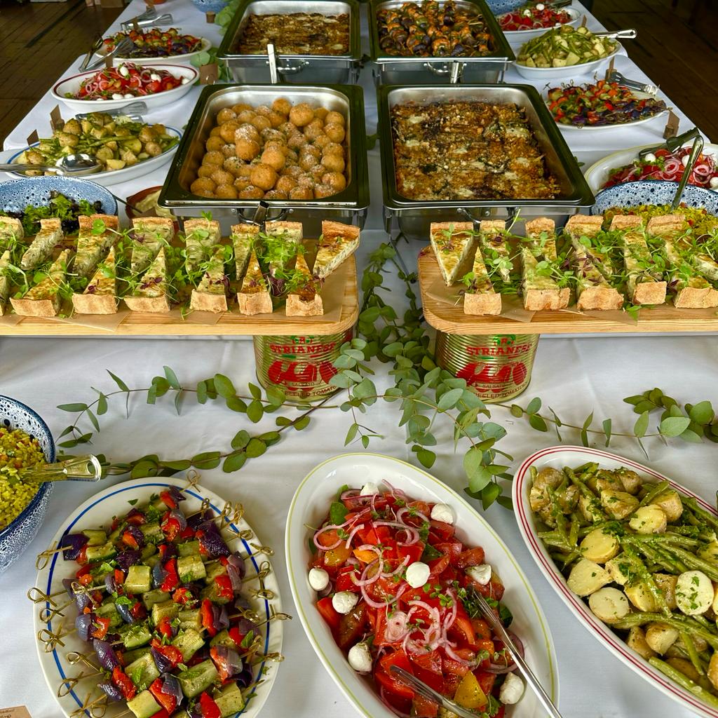 Gourmet buffet dishes of meat and vegetables on elevated stands and crockery, with full decorations on a white table.
