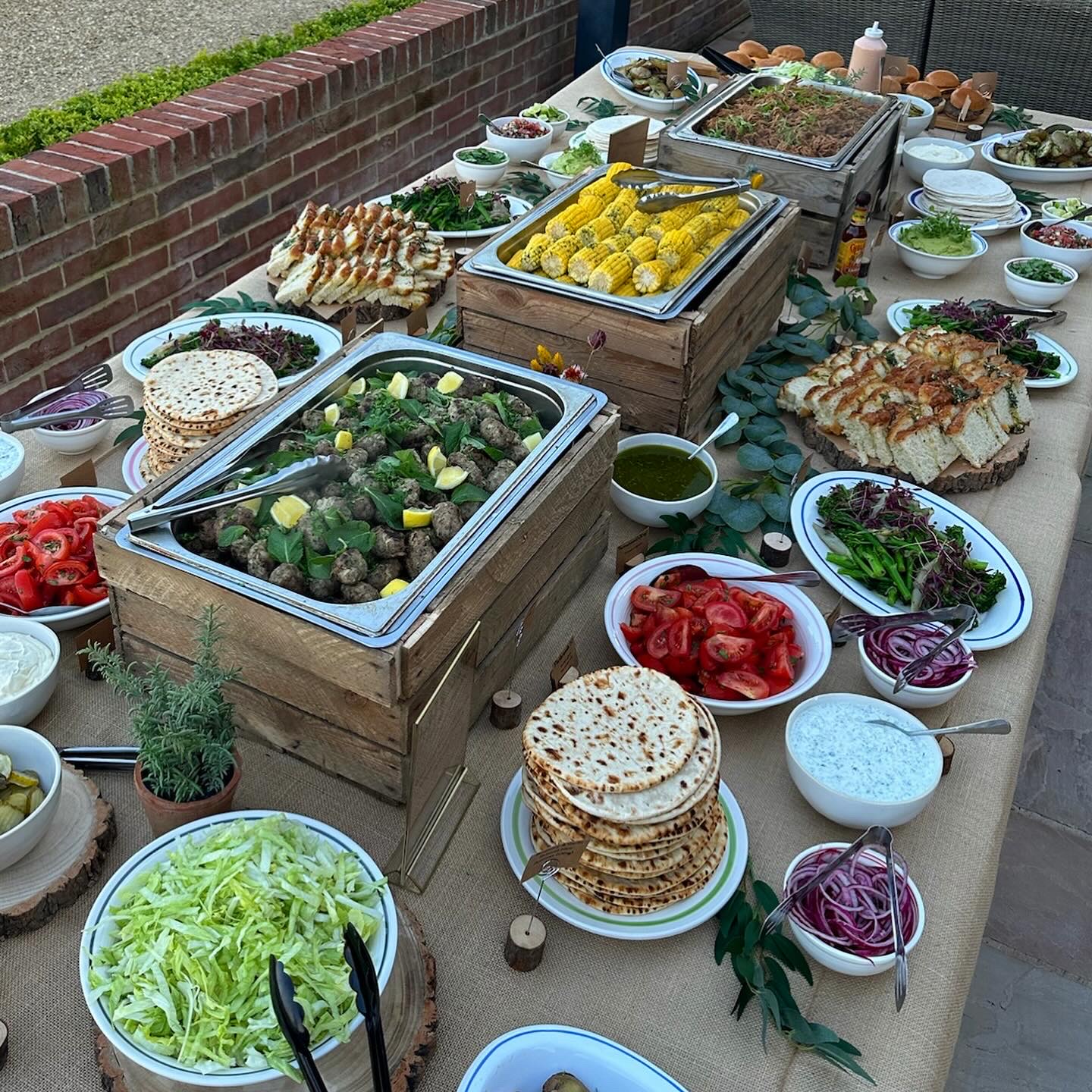 Outside BBQ catering table spread with accompaniments and side dishes to grilled meats.