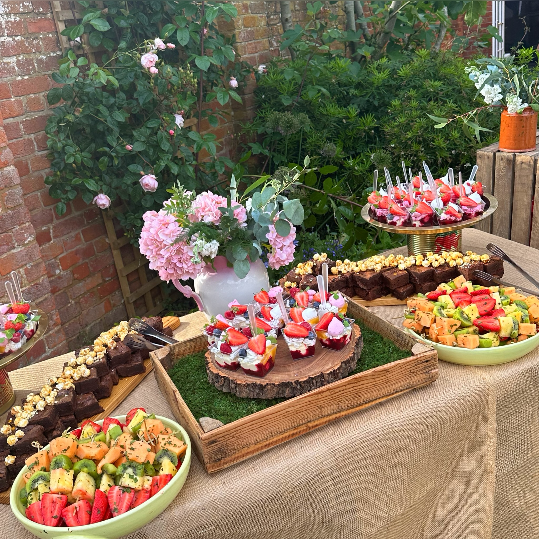 Outdoor BBQ dessert catering table, elegantly decorated with flowers and platters.